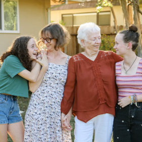 Grandma, mom and daughters look lovingly at each other in front of Sacramento home