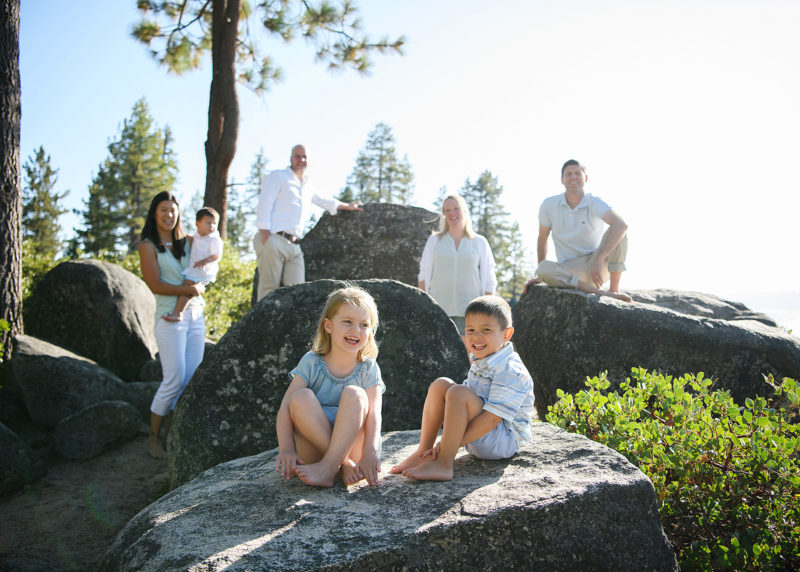 Boy and girl sitting on large rock with parents in background at Lake Tahoe