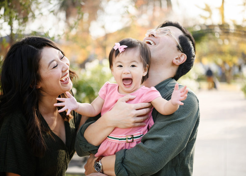 Mom and dad laugh while baby daughter opens her mouth wide at McKinley Park Rose Garden Sacramento