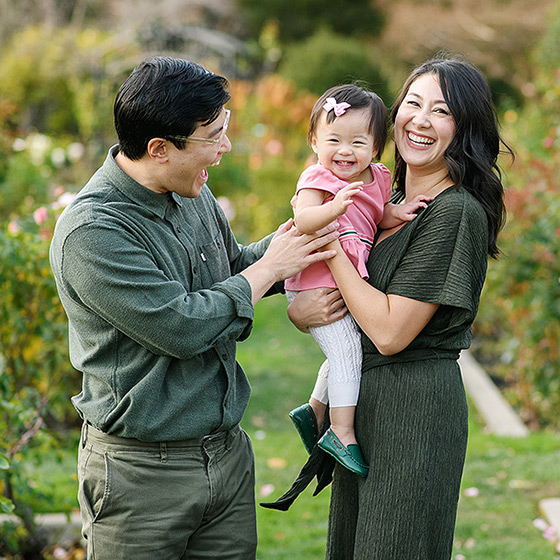 Mom and dad smiling and making toddler daughter laugh at McKinley Park Rose Garden Sacramento