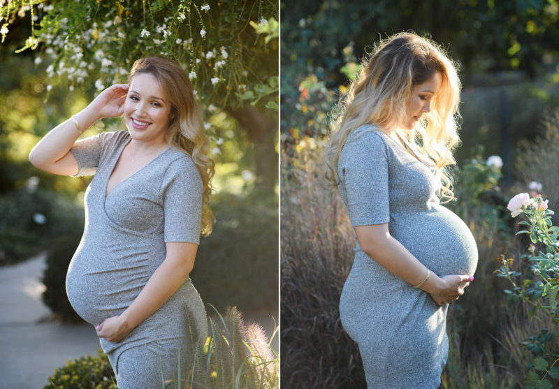 Pregnant woman wearing gray smiling and looking at baby bump with trees in the background