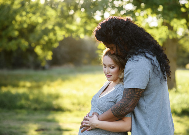 Pregnant woman and dad hugging and caressing baby bump outdoors in Davis