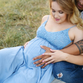 Pregnant woman and man touching baby bump while sitting on grass