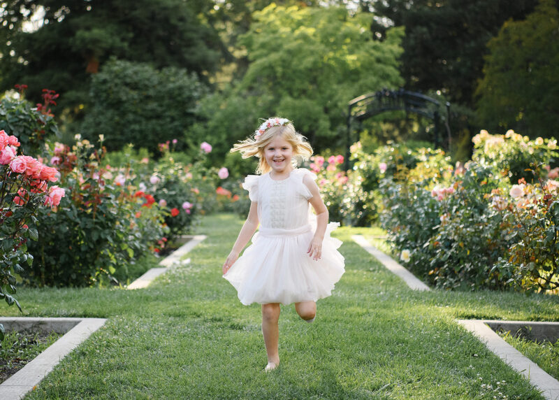 Little girl in white dress runs on grass at McKinley Park Rose Garden