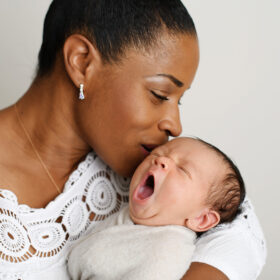 Black mom kissing newborn baby that is yawning in Sacramento studio