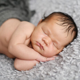 Newborn baby sleeping on hands lying on fuzzy gray blanket in Sacramento studio