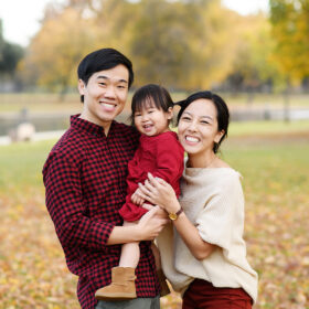 Mom and dad holding daughter and smiling with fall leaves on the ground in Sacramento Rancho Cordova