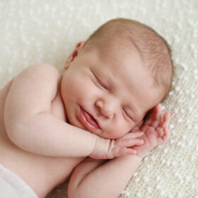 Newborn baby girl smiling in her sleep while lying on fuzzy white blanket in studio