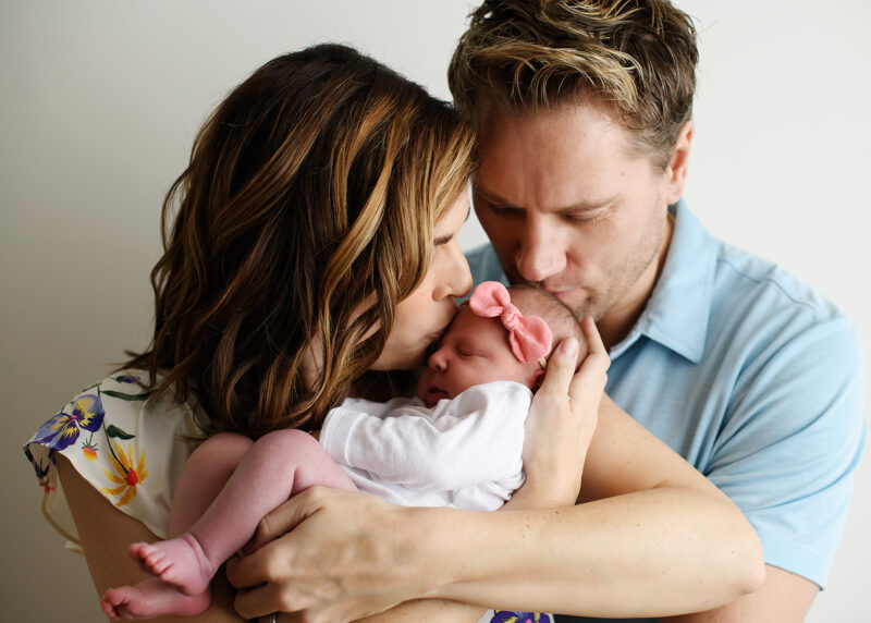 Mom and dad kissing newborn baby girl on head in Sacramento studio