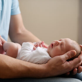 Dad holding sleeping newborn baby daughter in lap in studio