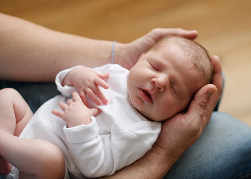 Close up of sleeping newborn baby girl being held by dad on his lap
