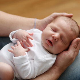 Newborn baby girl sleeping and being held in daddy’s arms aerial view
