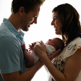 Mom and dad soft silhouette holding newborn baby girl and smiling in Sacramento studio