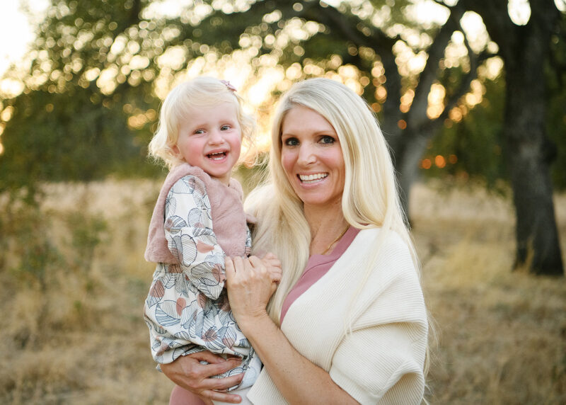 Mom holding toddler daughter and smiling with dry grass background in Folsom