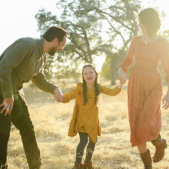Daughter laughing while holding hands with mom and dad in Folsom dry grass during sunset