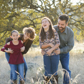 Family laughing and hugging on dry yellow grass in Cameron Park Sacramento