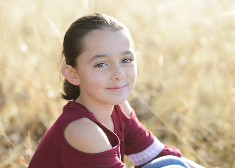 Girl smiling directly at camera close up with dry grass background in Cameron Park