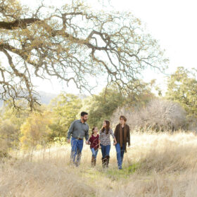 Family walking through dry grass under a large tree in Cameron Park