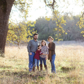 Family picture under a large tree while standing on dry grass in Cameron Park