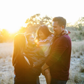 Mom and dad holding son and daughter and smiling directly in golden sunset light