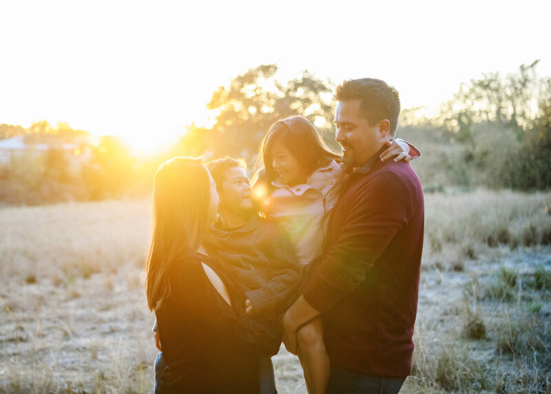 Mom and dad holding son and daughter and smiling directly in golden sunset light
