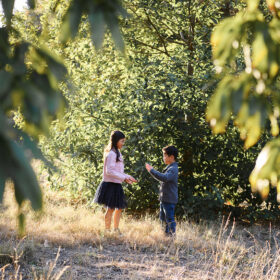 Brother and sister playing patty cake in between trees in Davis