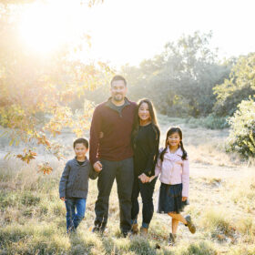 Mom and dad and brother and sister hold hands under the sunset light on dry grass in Davis