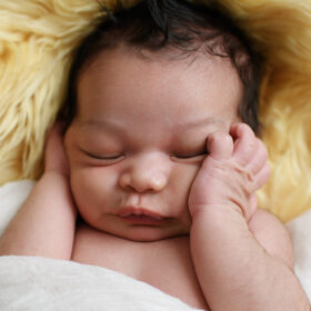 Newborn baby boy sleeping and putting his hands on his face while lying on shaggy blanket