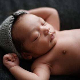 Newborn baby boy sleeping with hands up wearing a gray knit beanie