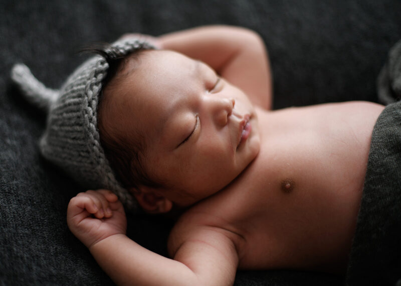 Newborn baby boy sleeping with hands up wearing a gray knit beanie