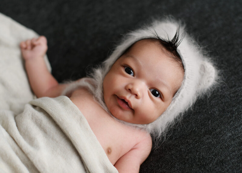 Newborn baby boy wearing fuzzy bonnet looking directly at camera