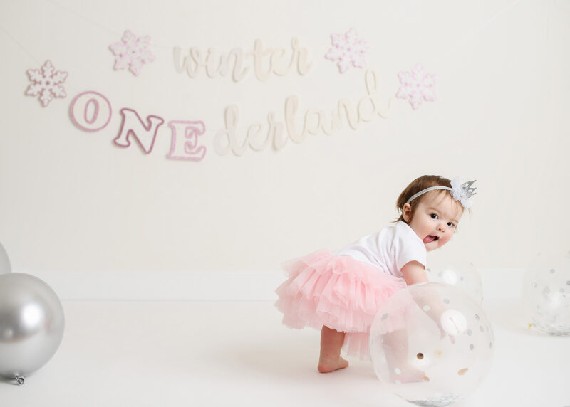 Baby girl in tutu sticking out her tongue and grabbing a balloon in Sacramento studio