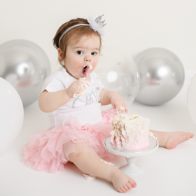 Baby girl in pink tutu eating and smashing her birthday cake in Sacramento studio