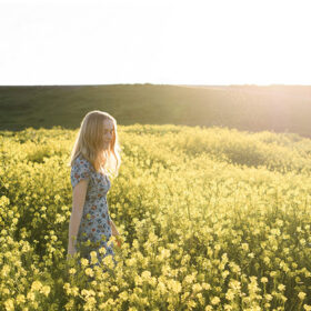 Teenage girl walking through yellow wildflowers with sun in her hair in Sacramento