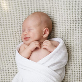 Newborn baby boy in white swaddle smiling in his sleep in Sacramento home