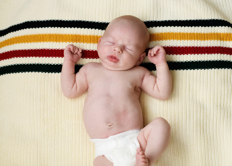 Newborn baby boy in diaper sleeping on retro pattern blanket in Sacramento home lifestyle session