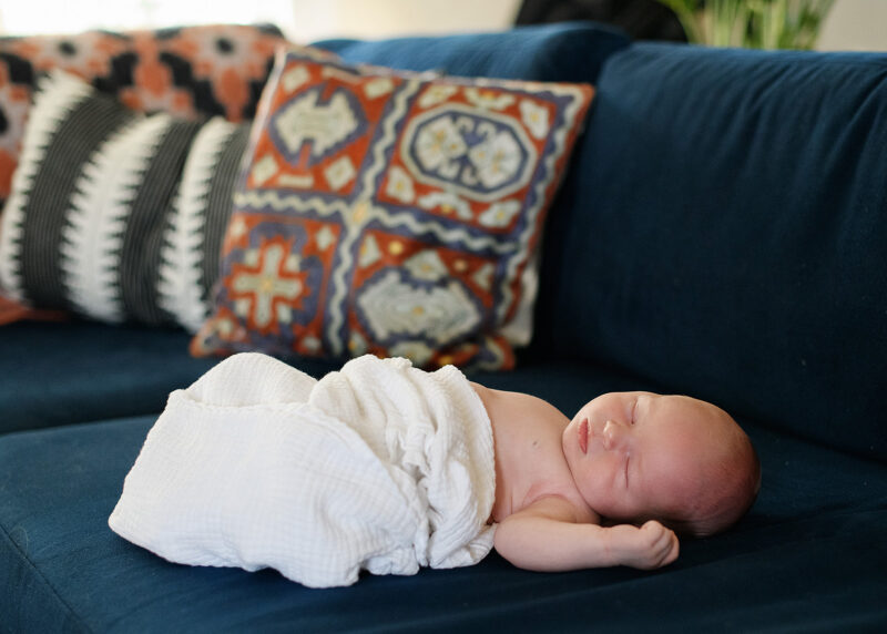 Baby boy in white swaddle sleeping on blue couch with pattern throw pillow in Sacramento home