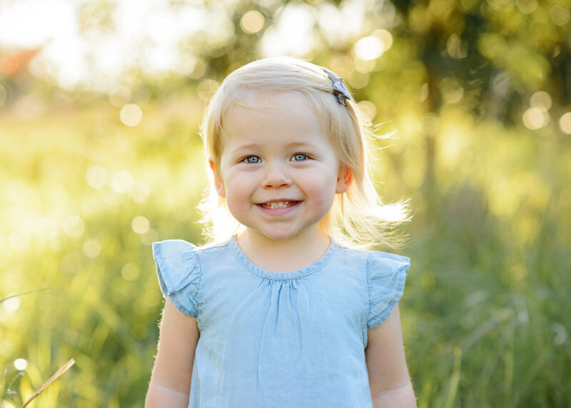 Toddler girl smiling directly at camera with trees and grass in background Sacramento