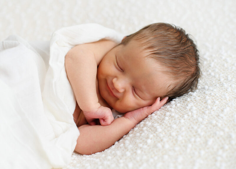 Sleeping newborn baby lying on fuzzy white blanket in Sacramento studio