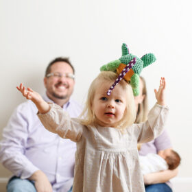 Toddler girl throwing colorful toy in air as mom and dad watch in background in Sacramento studio