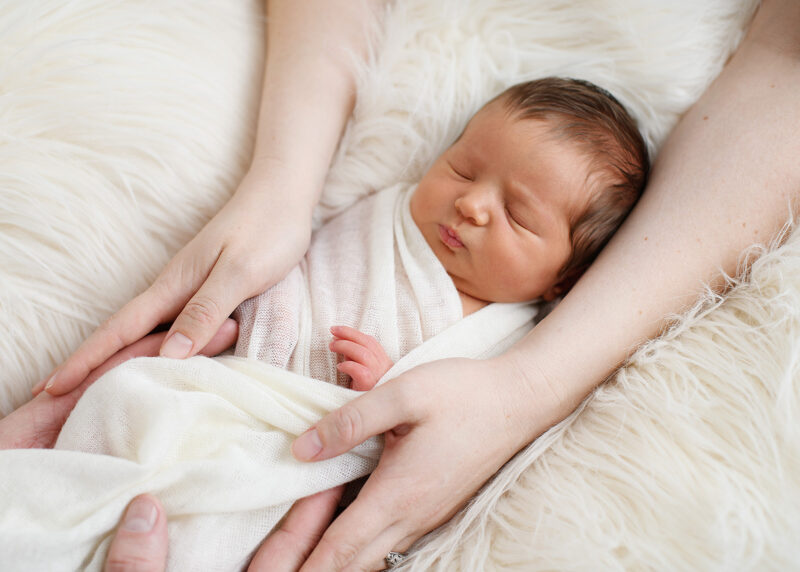 Sleeping newborn baby being cradled by mom's hands on sherpa throw in Sacramento studio