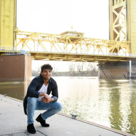 High school senior boy squatting at Sacramento waterfront and Tower Bridge in background