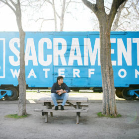 High school senior boy sitting on bench in front of blue train in Old Sacramento