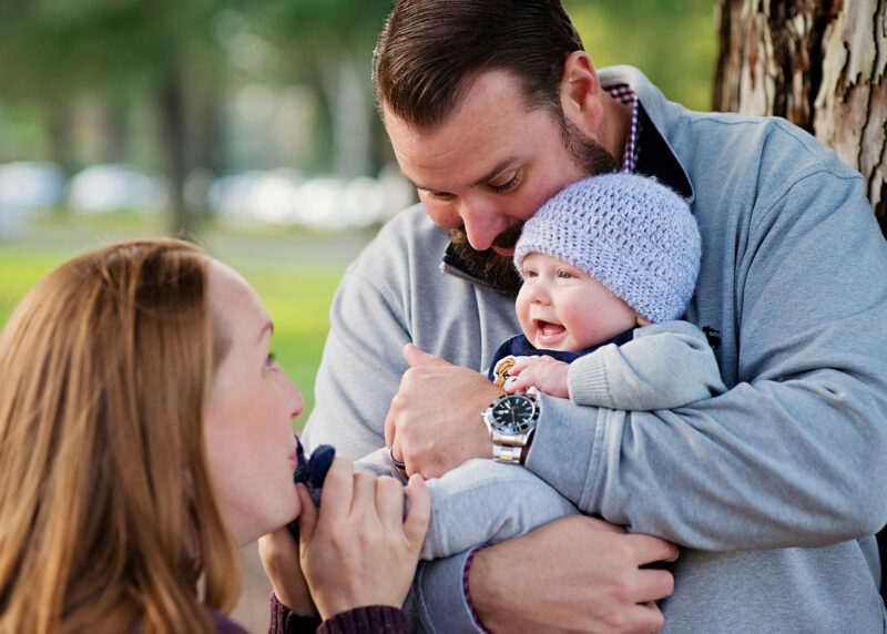 Mom makes baby boy smile as dad holds him outdoors