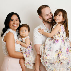 Mom holds one year old daughter while dad holds big sister dressed in florals in Sacramento studio