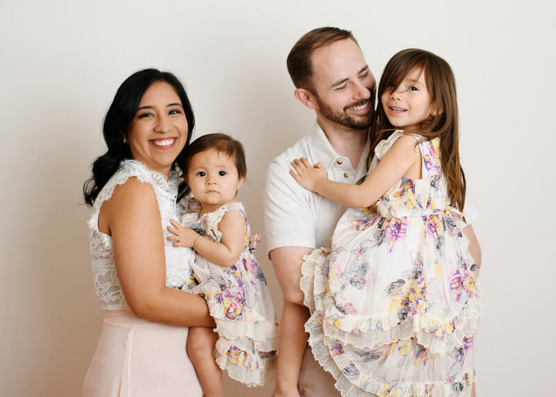 Mom holds one year old daughter while dad holds big sister dressed in florals in Sacramento studio