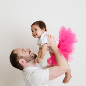 Dad holds one year old daughter up high dressed in pink tutu in Sacramento studio