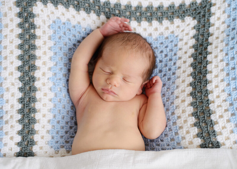 Sleeping newborn baby with hands up on blue quilted blanket 