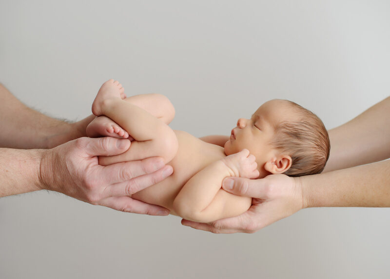 Newborn baby being held by mom and dad against white wall in Sacramento studio