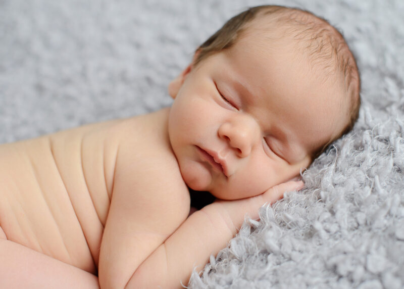 Newborn baby sleeping on hands on gray blanket in Sacramento studio